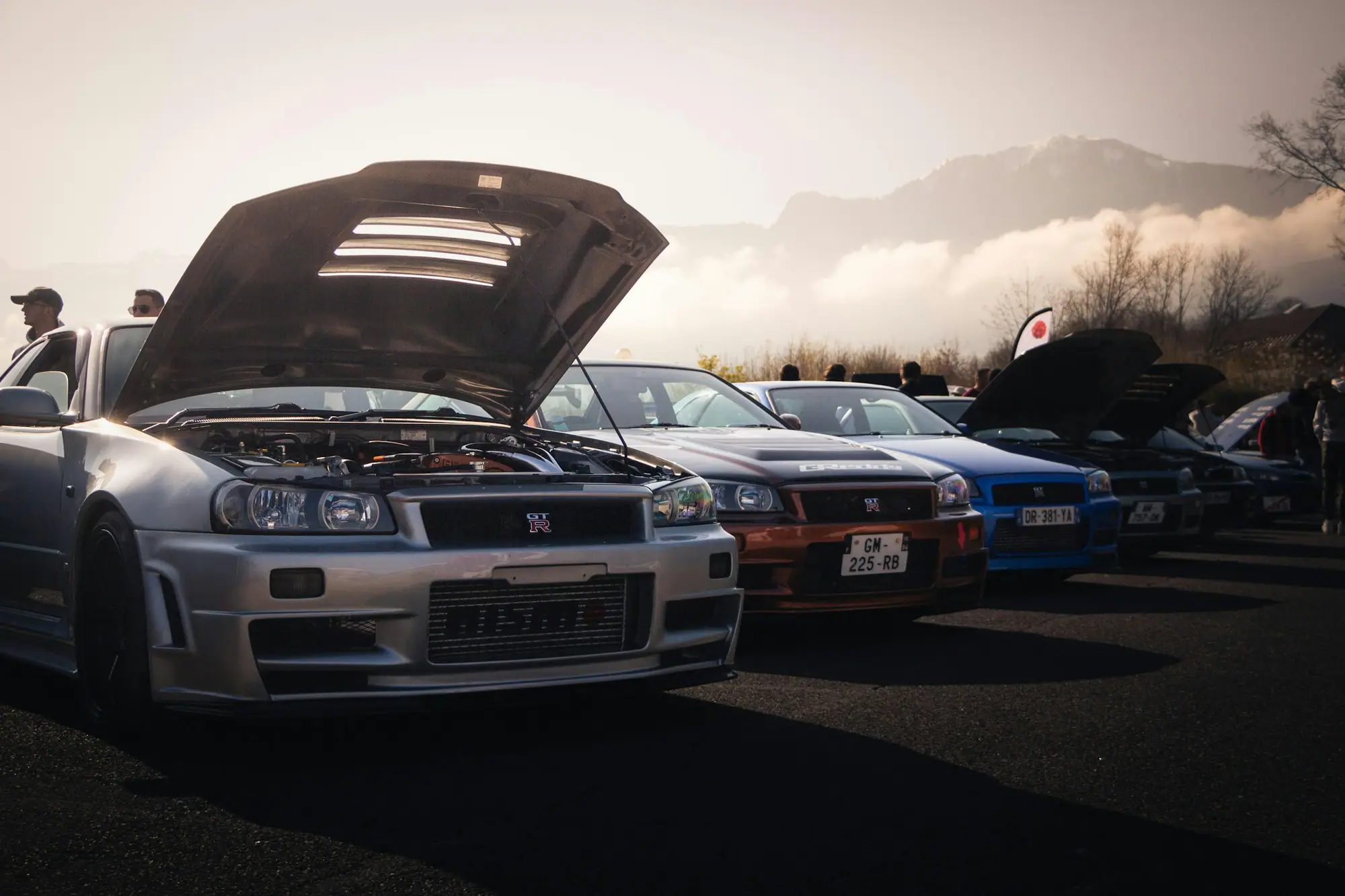 Nissan Skyline GT-R R34s lined up with hoods open for inspection