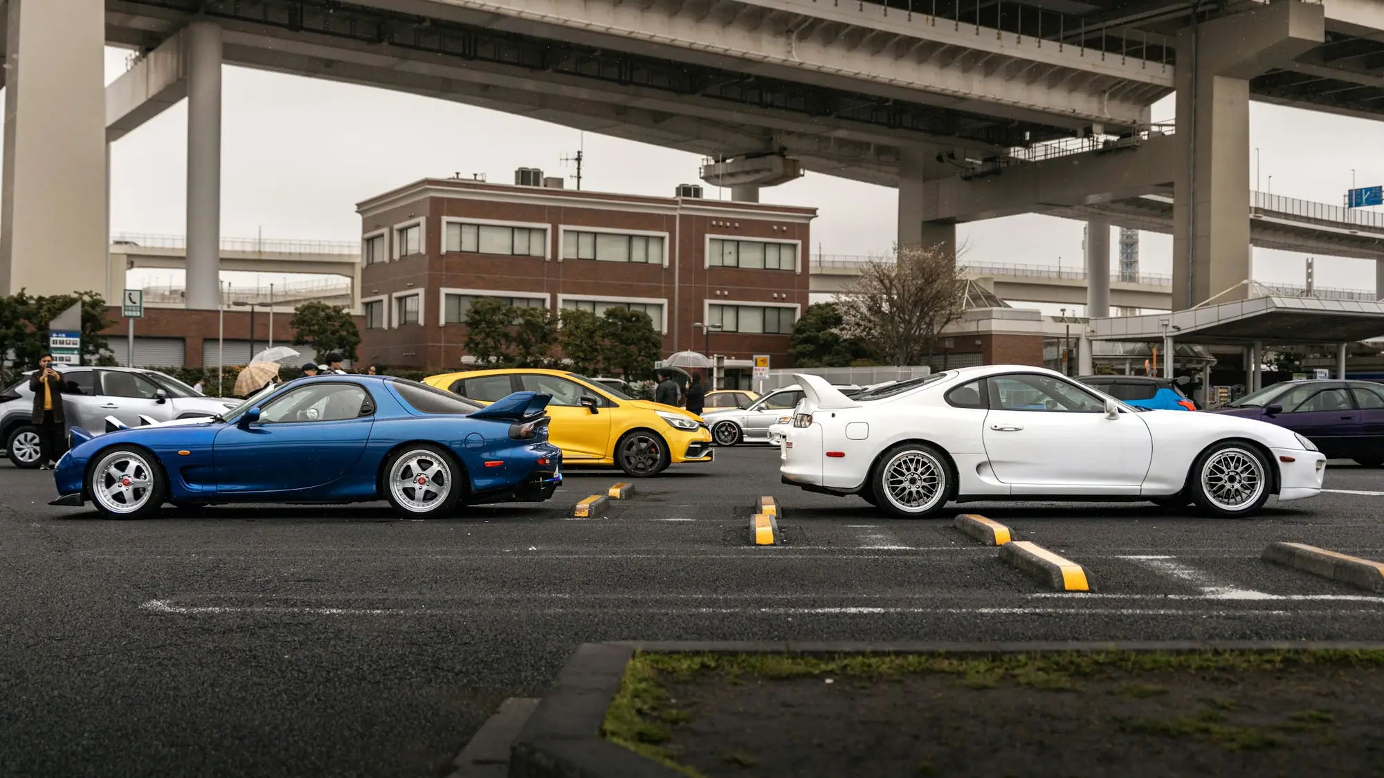Mazda RX-7, Toyota Supra and other JDM cars parked under an expressway in Japan